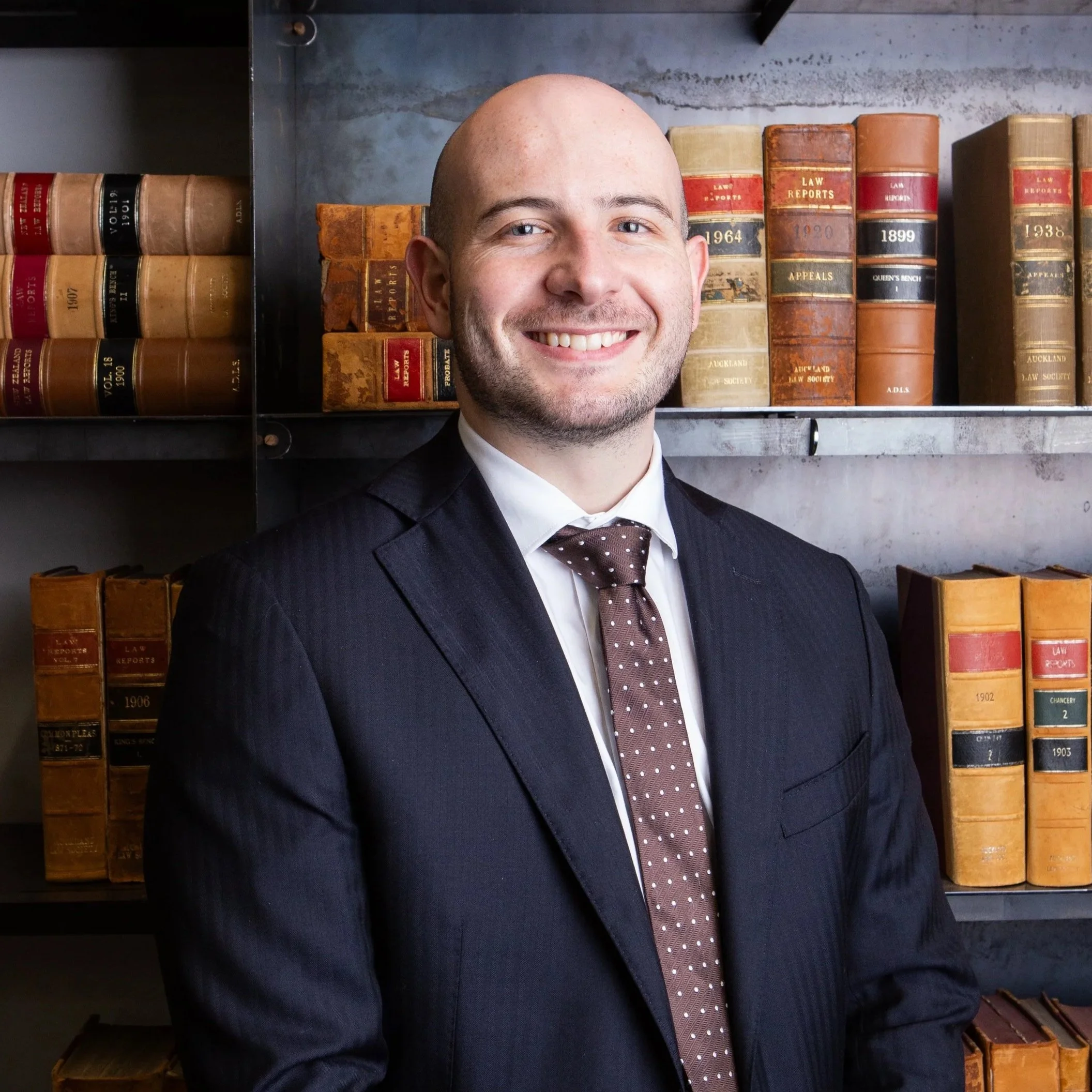 A man in a suit smiling in front of a bookshelf filled with old law books.