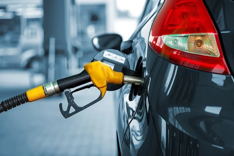 Close-up of a fuel nozzle filling a dark-colored car at a gas station.