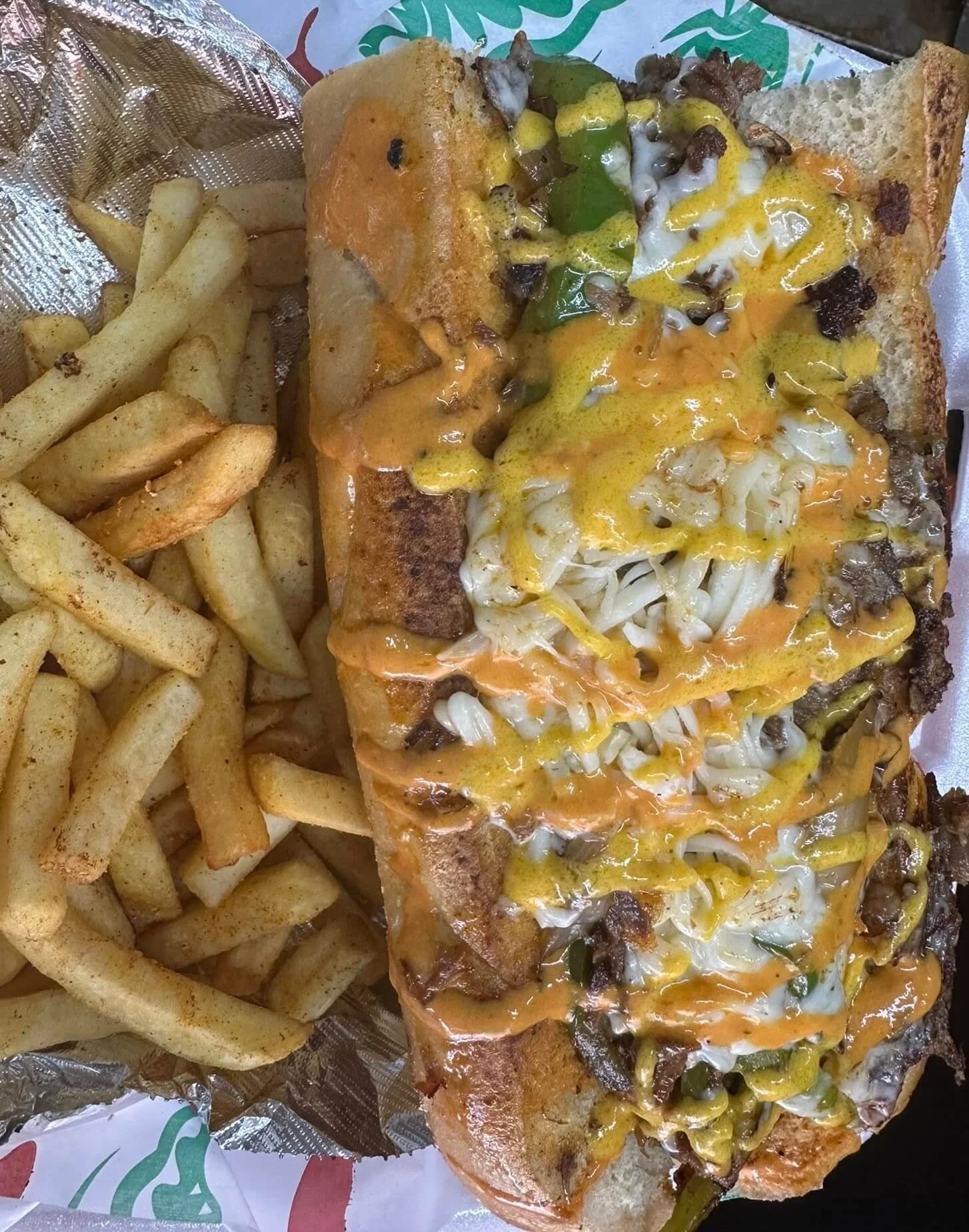 lapaisanita-starkville-philly-cheesesteak.jpg → Philly cheesesteak sandwich topped with melted cheese and sauce, served with fries.