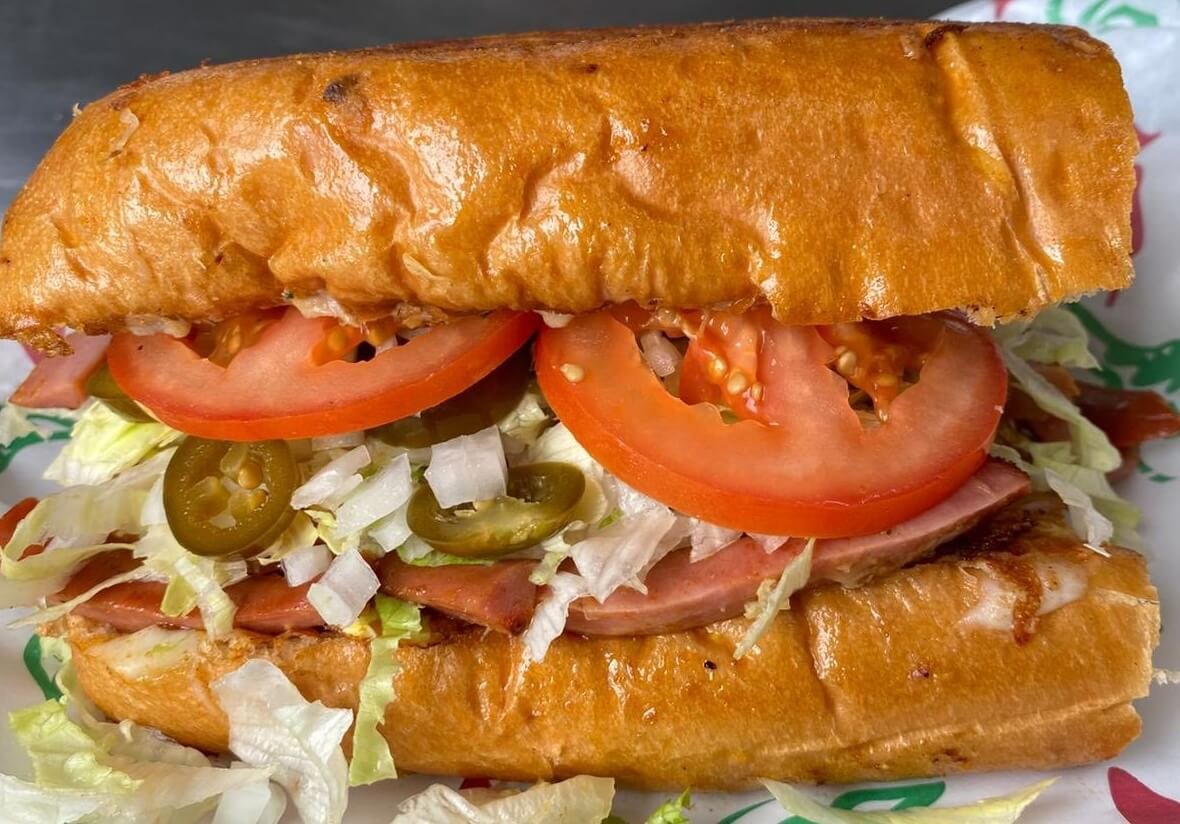 lapaisanita-starkville-sub-sandwich2.jpg → Close-up of La Paisanita sub sandwich with tomatoes, jalapeños, and shredded lettuce.