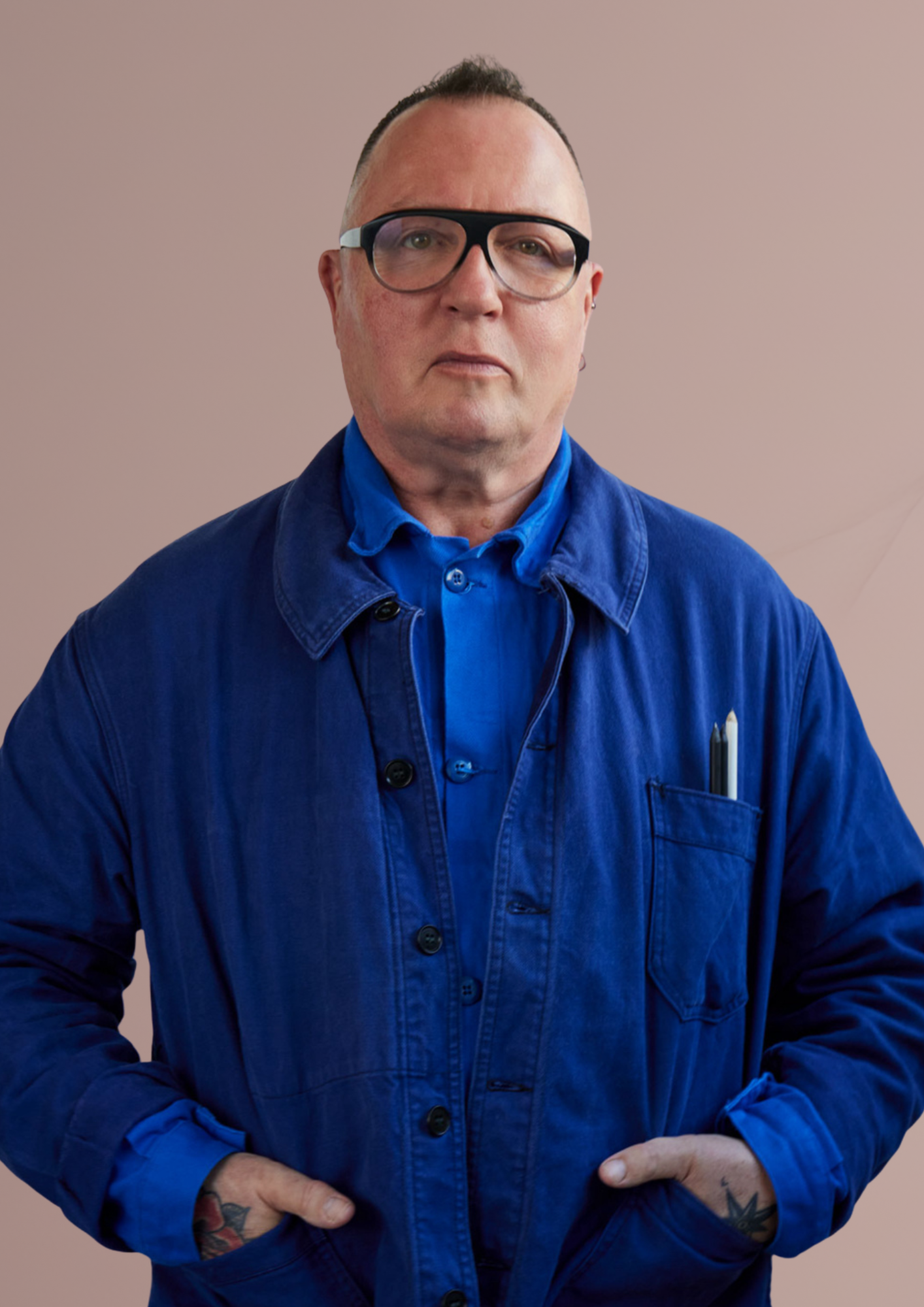 Serge is wearing glasses a blue jacket and shirt, standing with both hands in his pockets against a plain background.