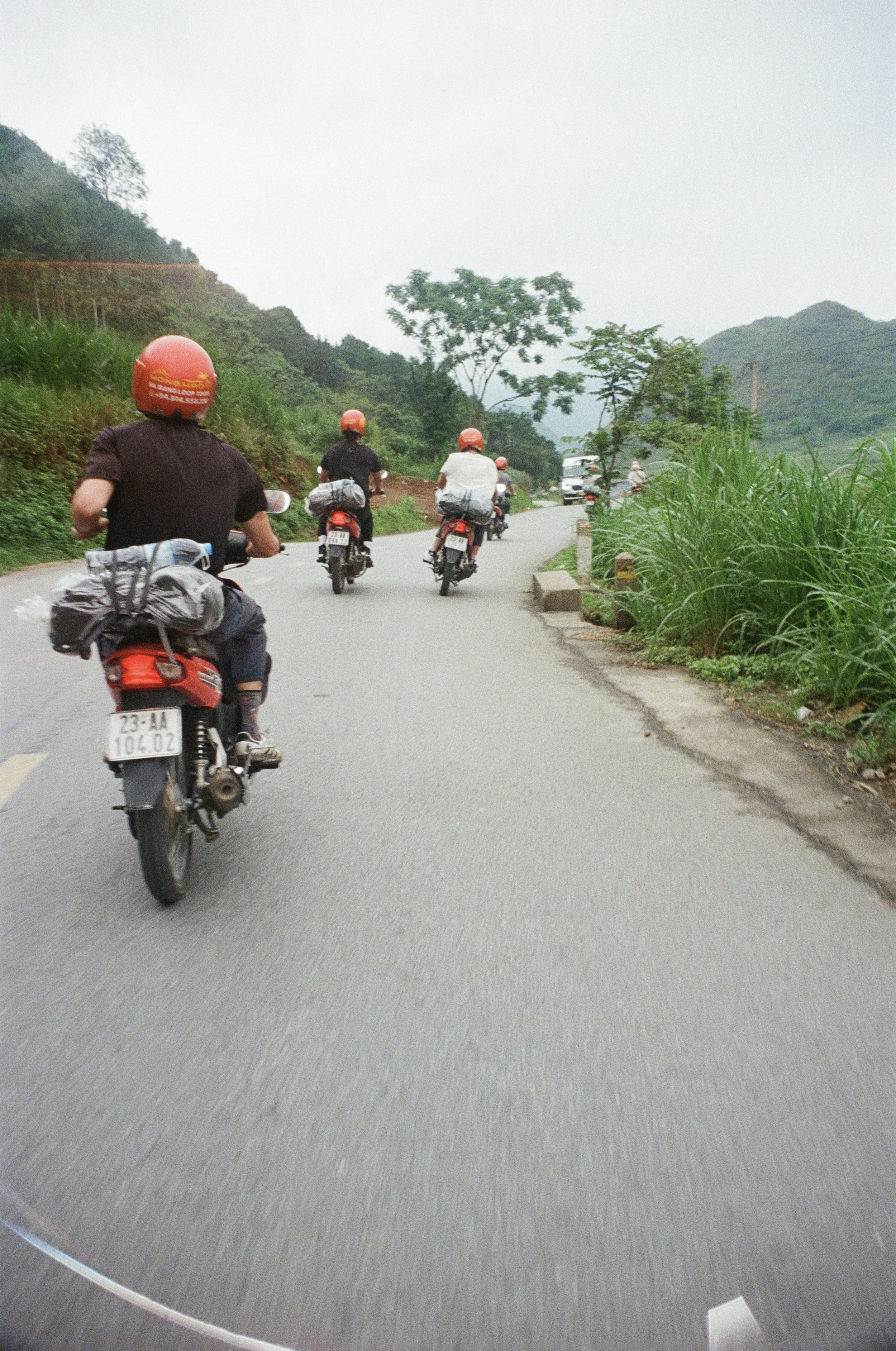 Motorcycles riding on a winding road through a hilly, green landscape.