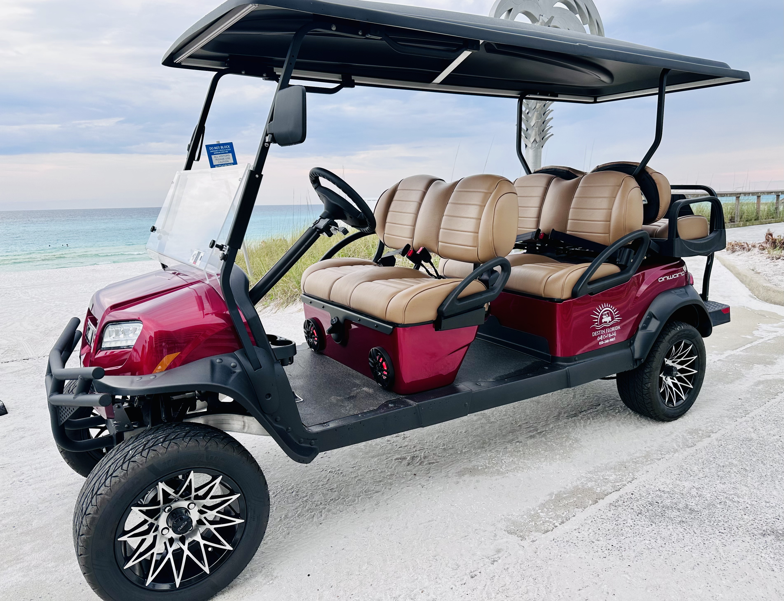 Red electric golf cart with tan seats parked on a sandy beach near the ocean.