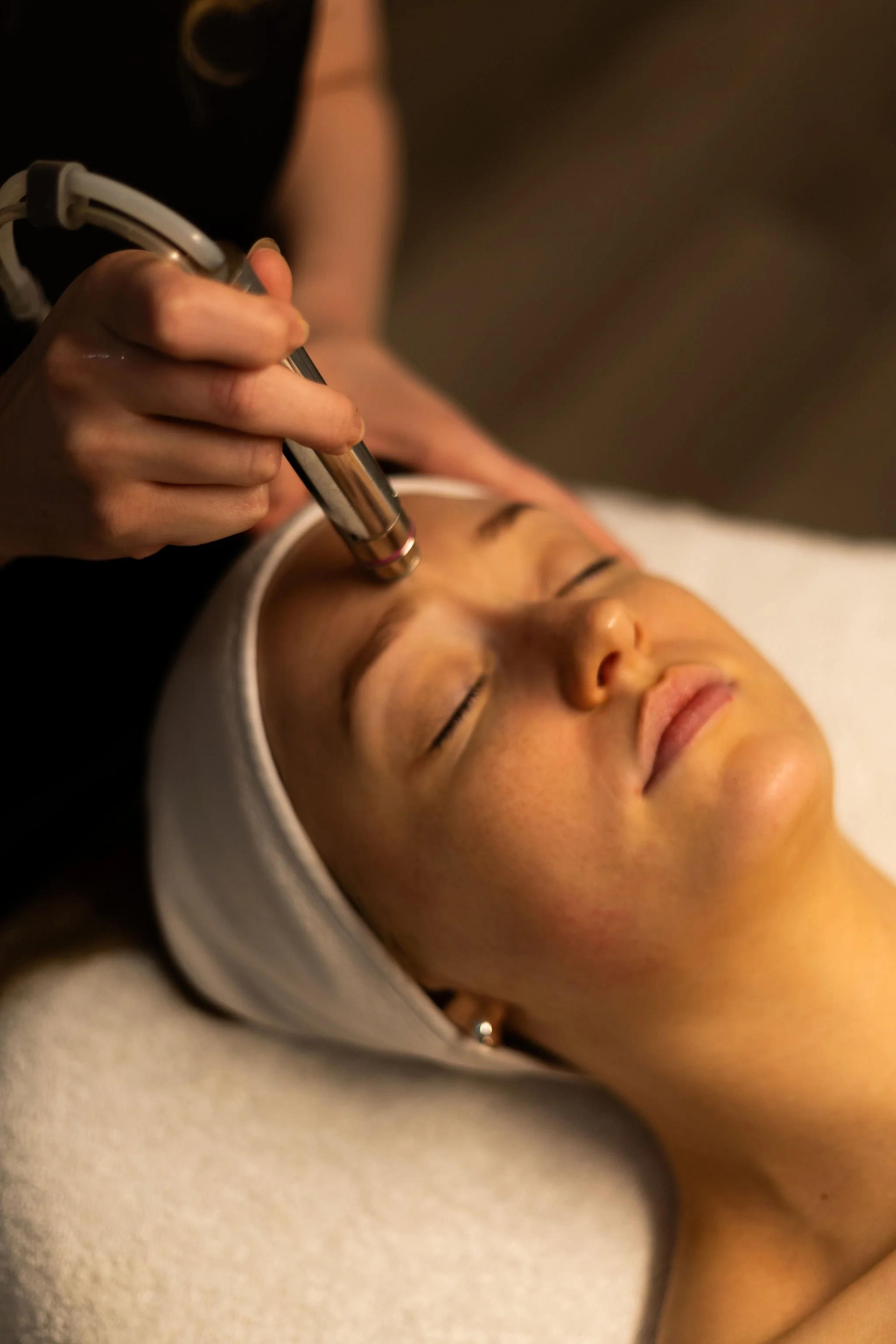 A woman receives a facial treatment with a handheld device by a professional in a spa or skincare clinic.