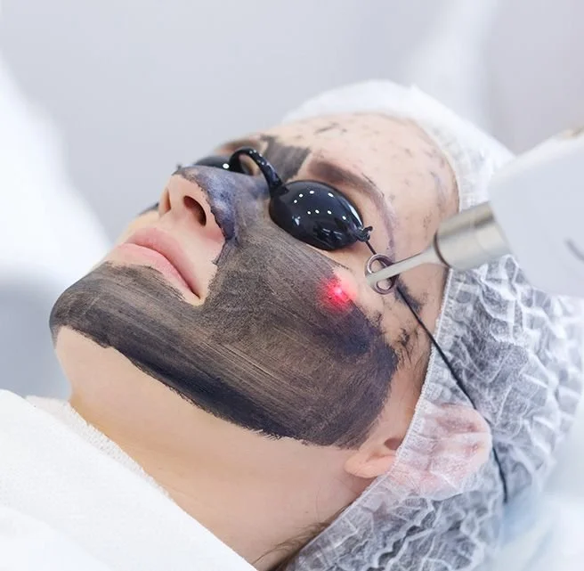Patient receiving laser facial treatment with protective glasses and a dark facial mask.
