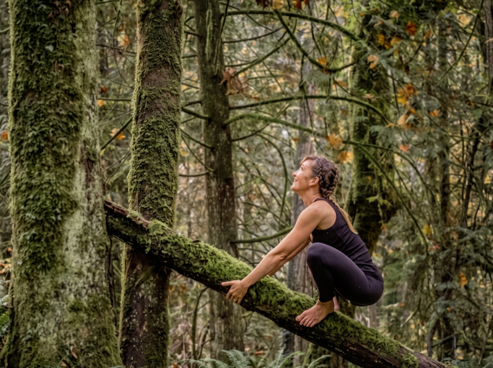 A white woman with braided hair practicing yoga on a moss-covered fallen tree in a pacific northwest forest