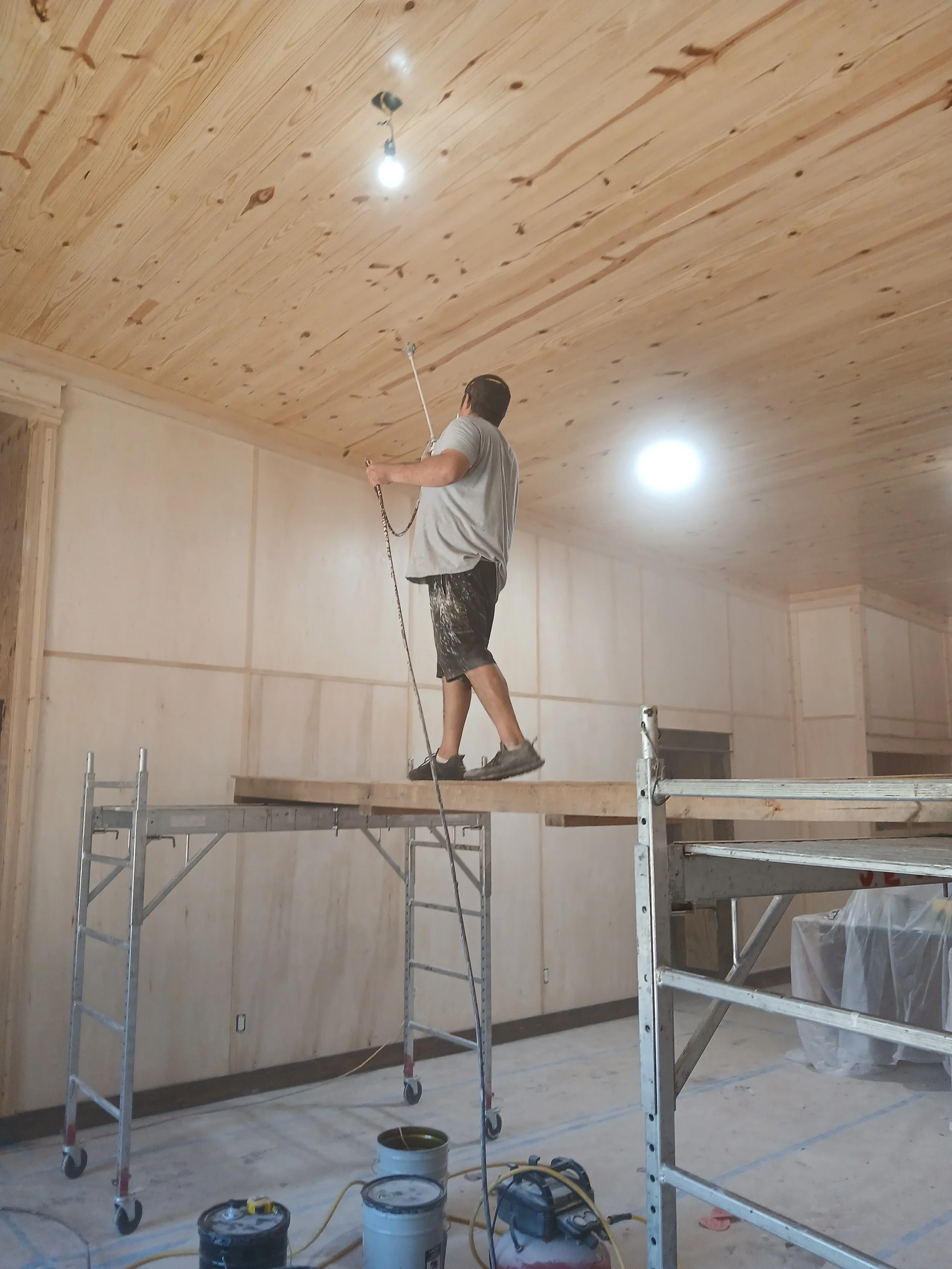 A man working on a scaffold, sanding or polishing a wooden ceiling in a room under construction.