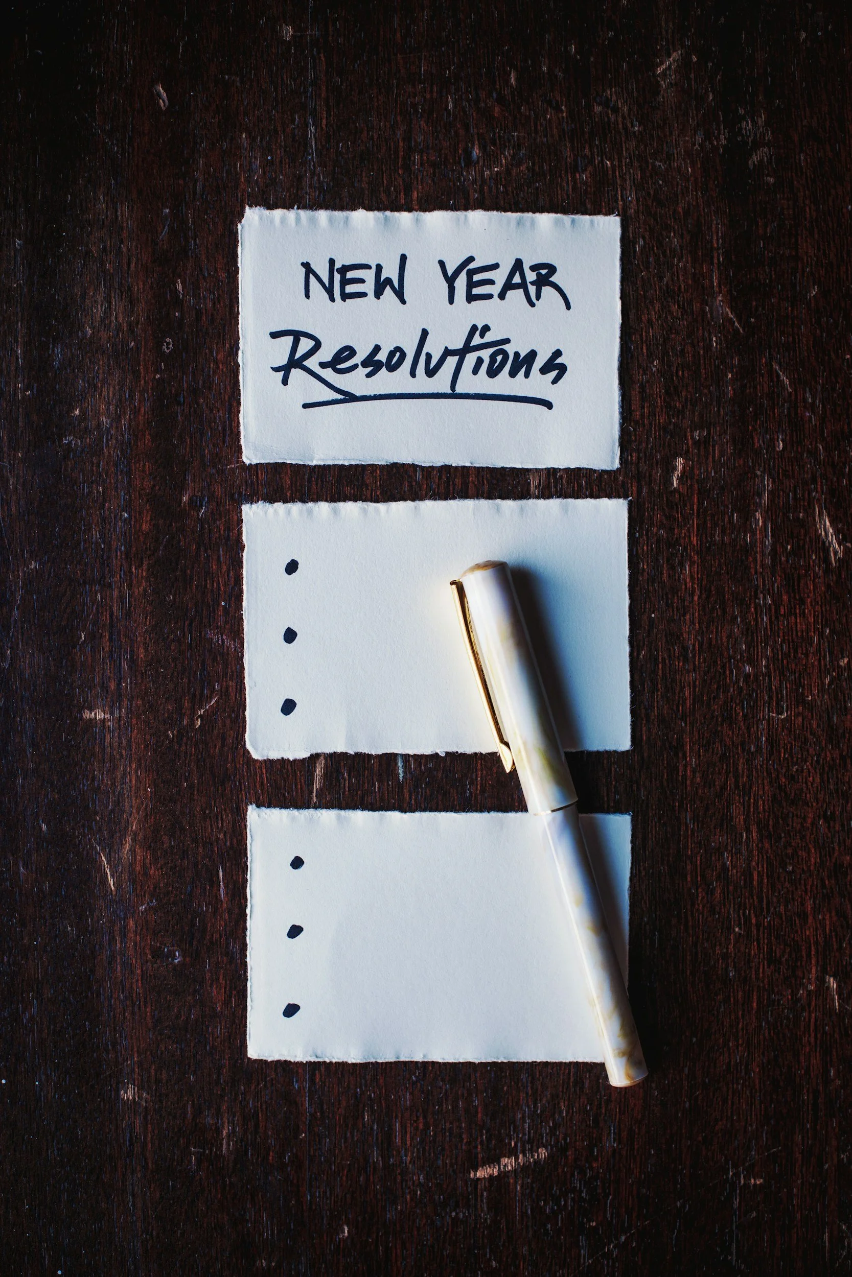 New Year's Resolution on white paper with black bullet points sitting on a wood desk