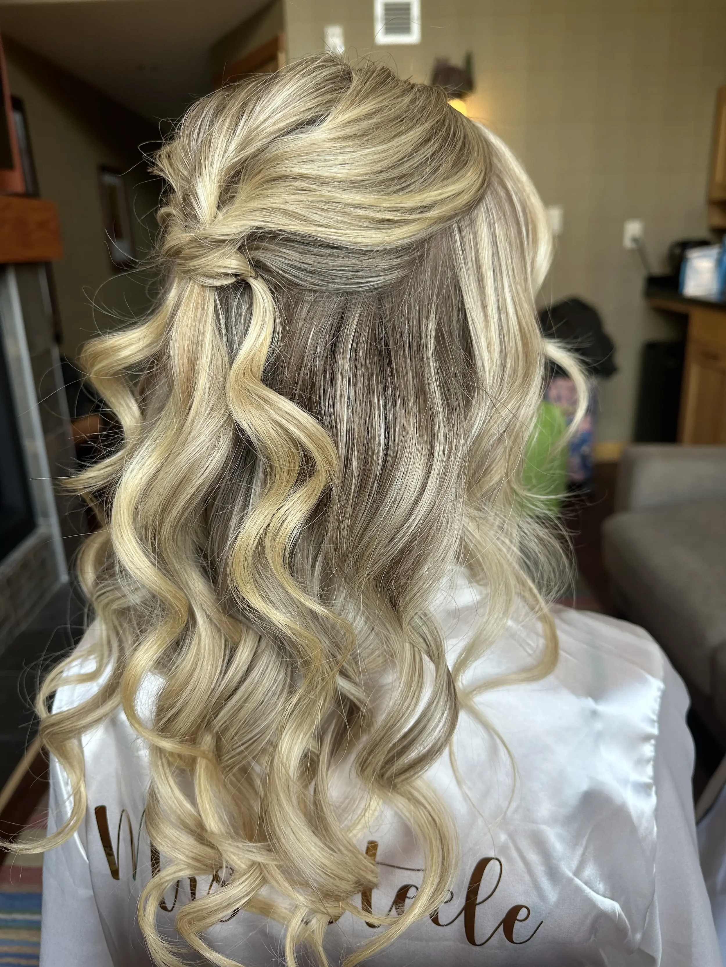 Blonde woman with styled curly hair seen from behind in a home setting.