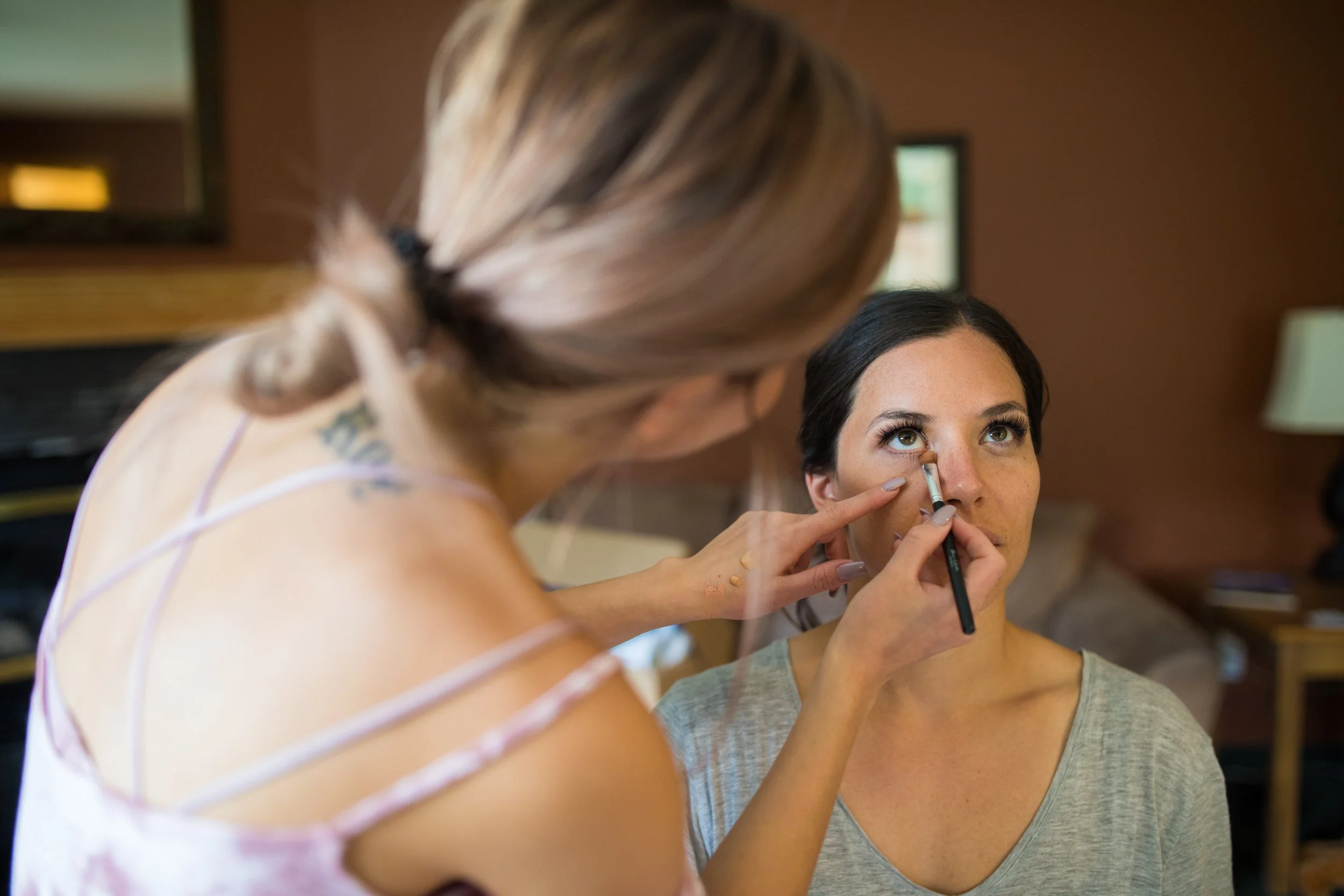 Makeup artist applying makeup to a woman with short dark hair, sitting indoors.