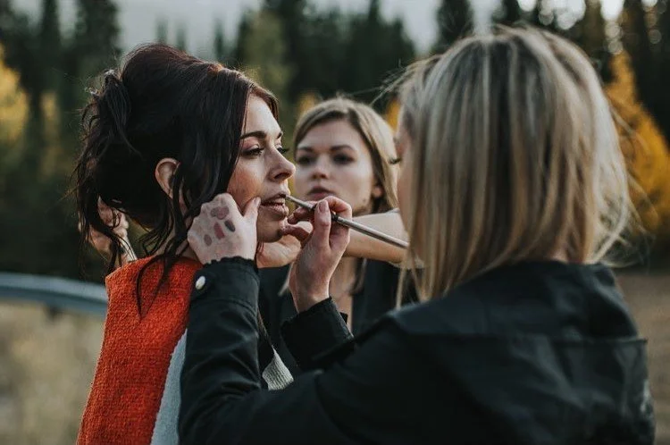 Women applying makeup outdoors with trees in the background