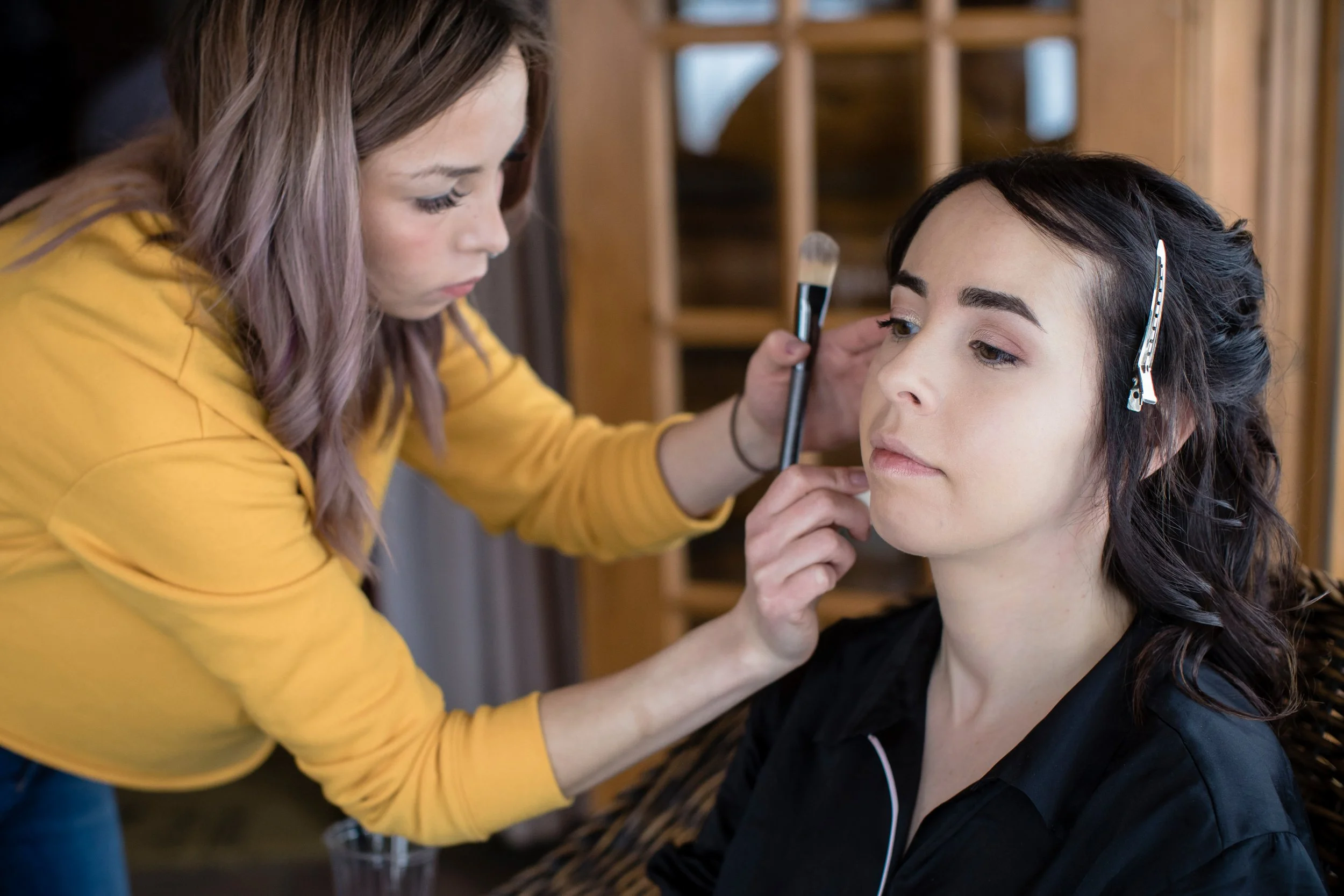 Makeup artist applies makeup to a woman's face in a salon.