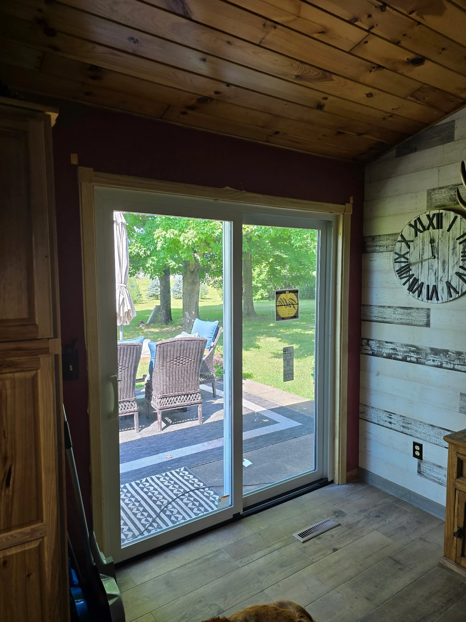 View from inside a room looking out through a sliding glass door onto an outdoor patio with chairs and trees.