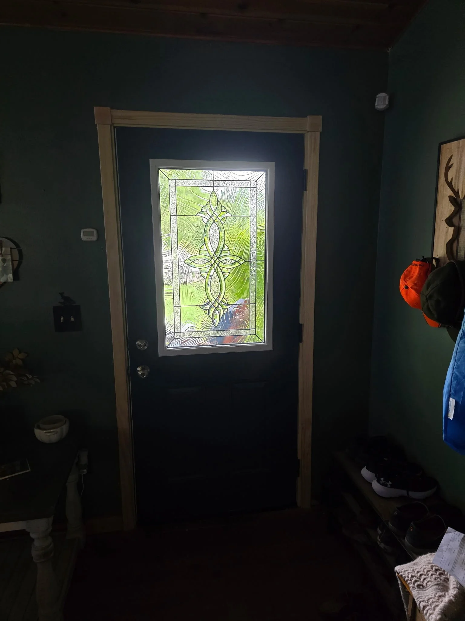 Front door with decorative glass window, surrounded by wood trim, in a home interior.