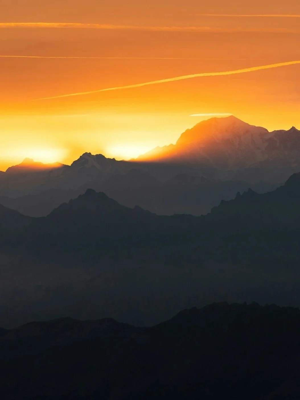 Sunset over a mountain range with orange and yellow sky and silhouettes of dark mountains.