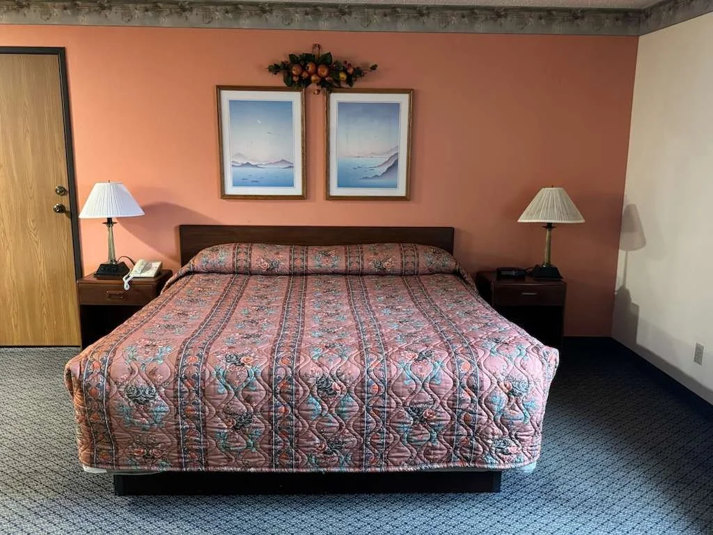 Hotel room with a bed, two nightstands with lamps, painting, and a floral wall decoration.