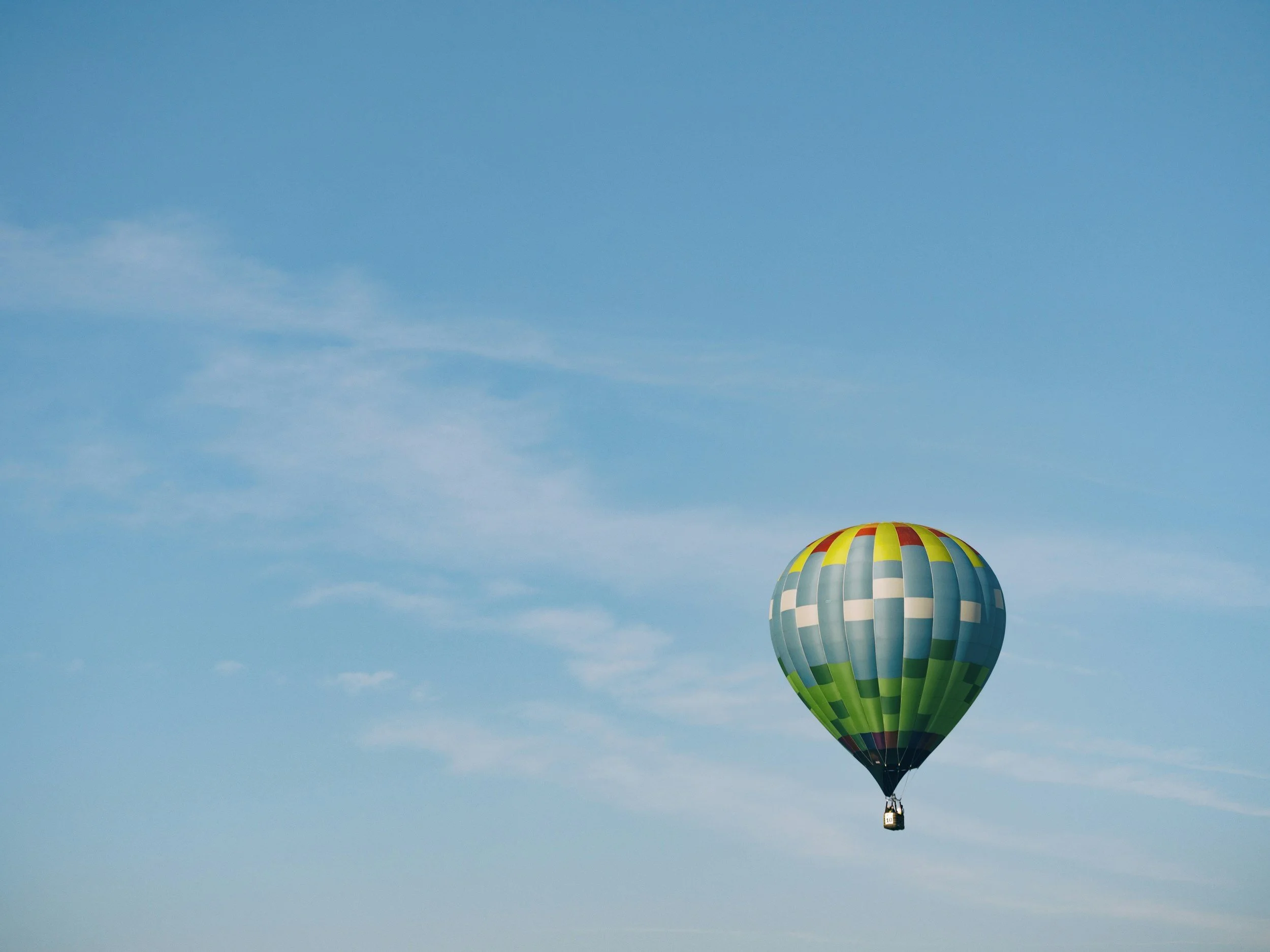 Colorful hot air balloon floating in a clear blue sky with light wispy clouds.