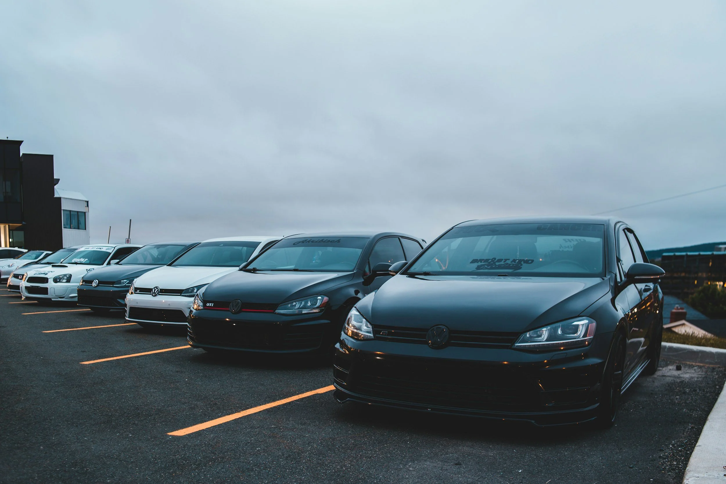 Multiple Volkswagen cars parked in a row in a parking lot on an overcast day.