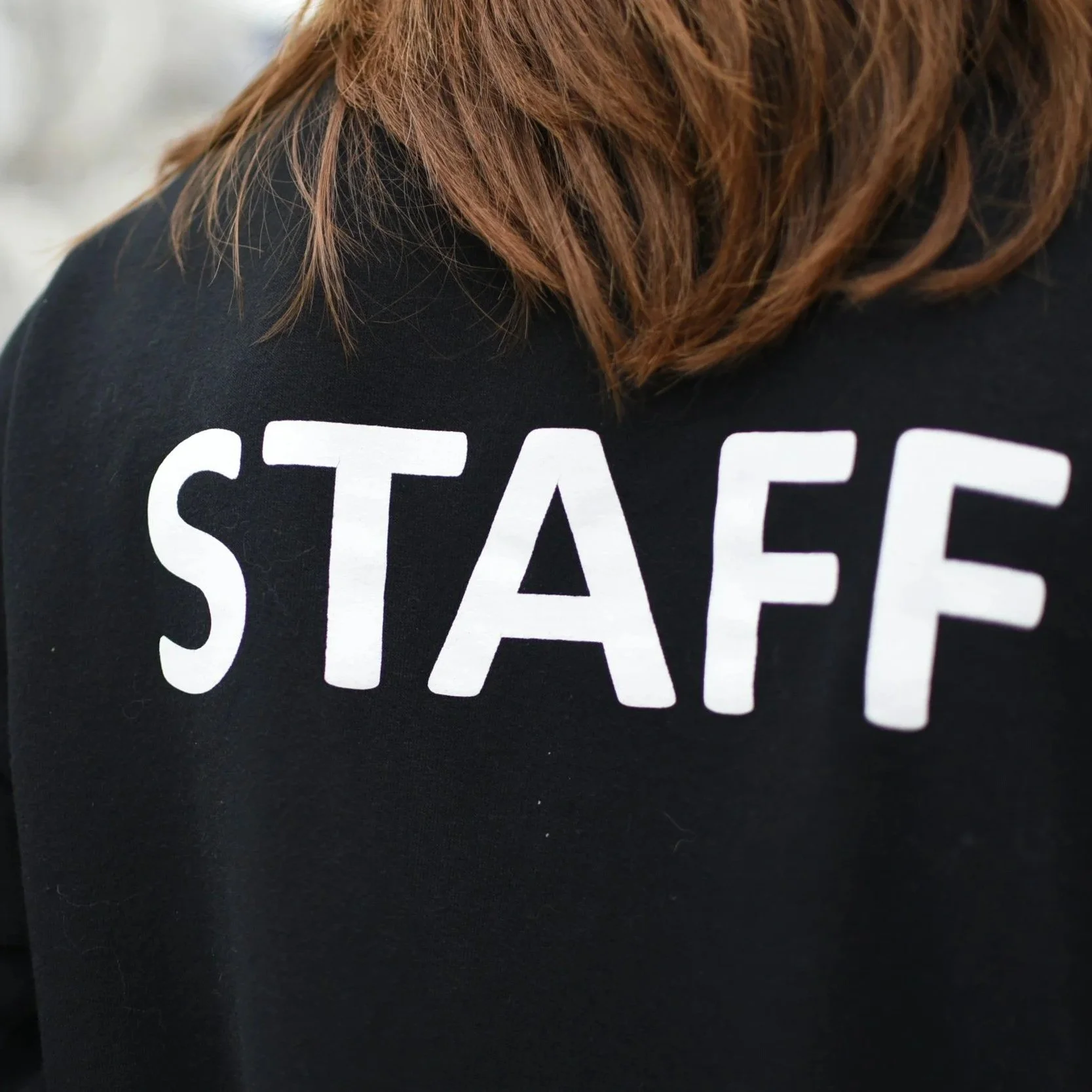 Close-up of a person's back wearing a black hoodie with the word 'STAFF' printed in large white letters.