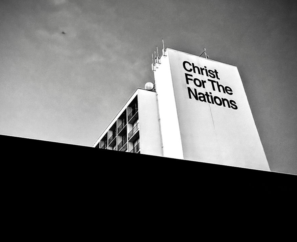 A black and white photo of a tall building with a large sign that reads "Christ For The Nations" on the side.