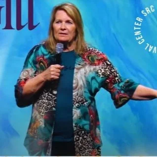 Woman speaking at a conference, holding a microphone, with a blue background.