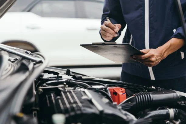 A person is inspecting a car engine and writing notes on a clipboard.