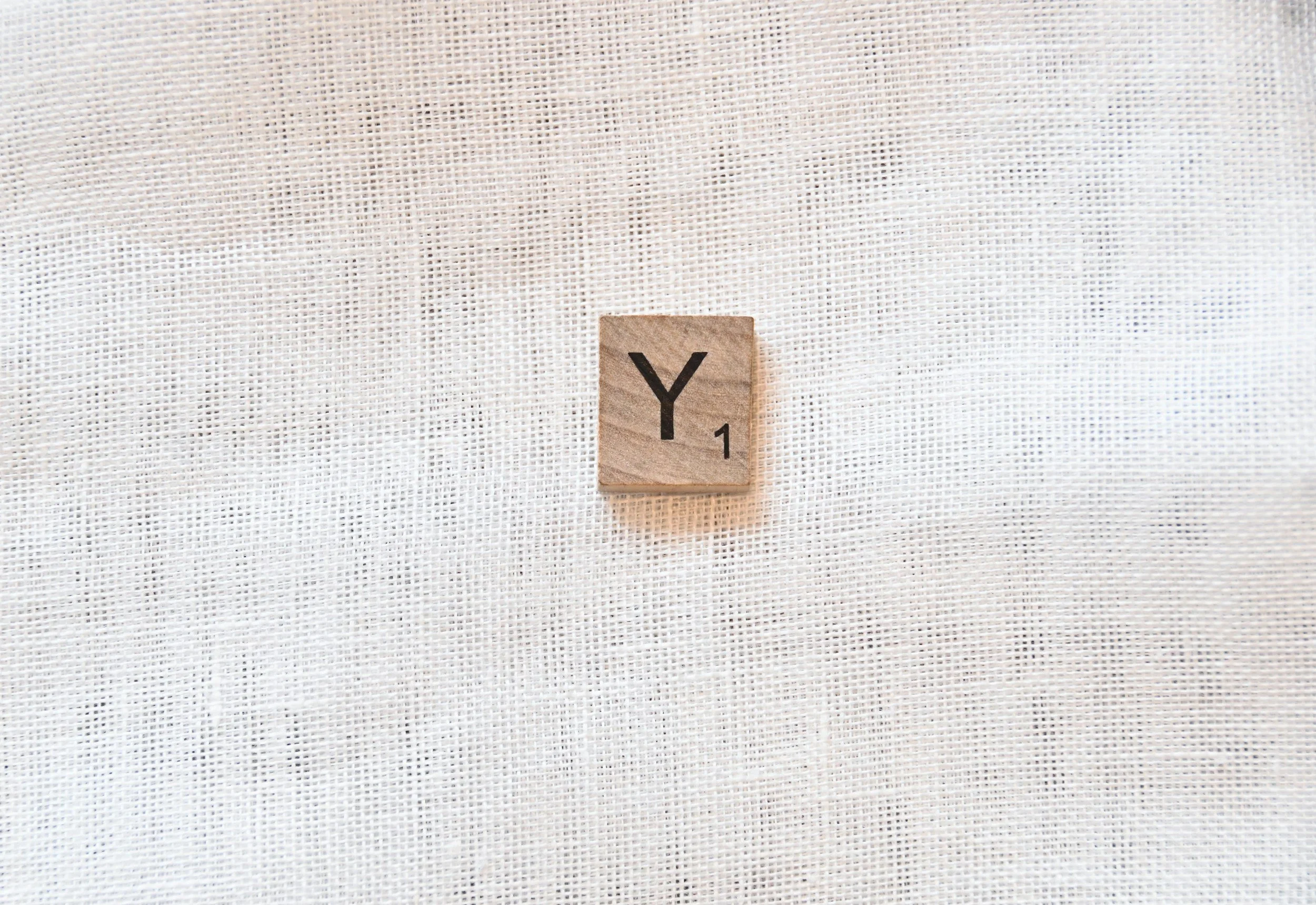 Scrabble tile with the letter 'Y' on a light fabric background.