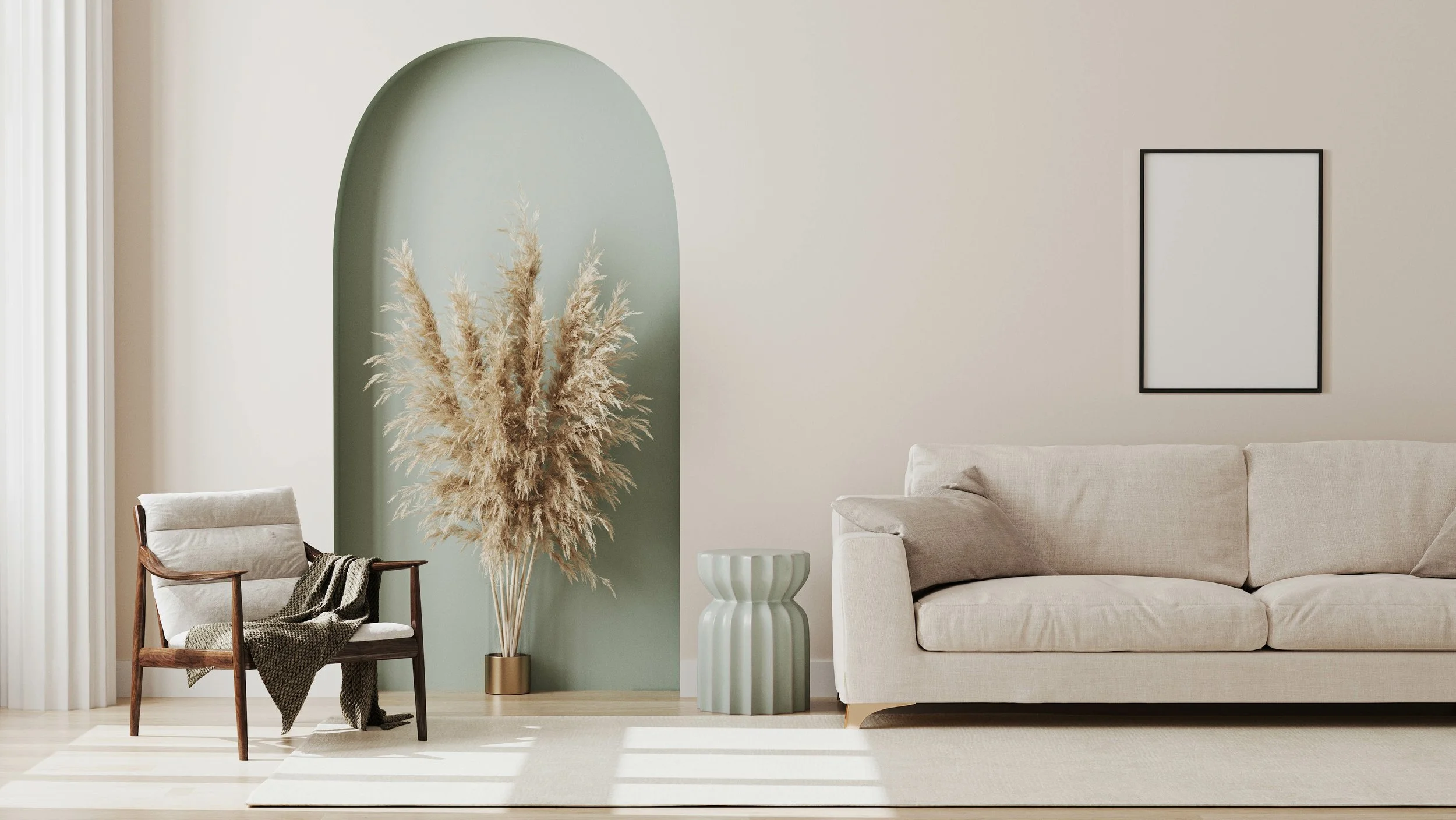 A minimalist living room with a beige sofa, a framed blank picture, a light green vase, and a wooden chair with a blanket, all on a light rug, with a green accent wall and a pampas grass arrangement.