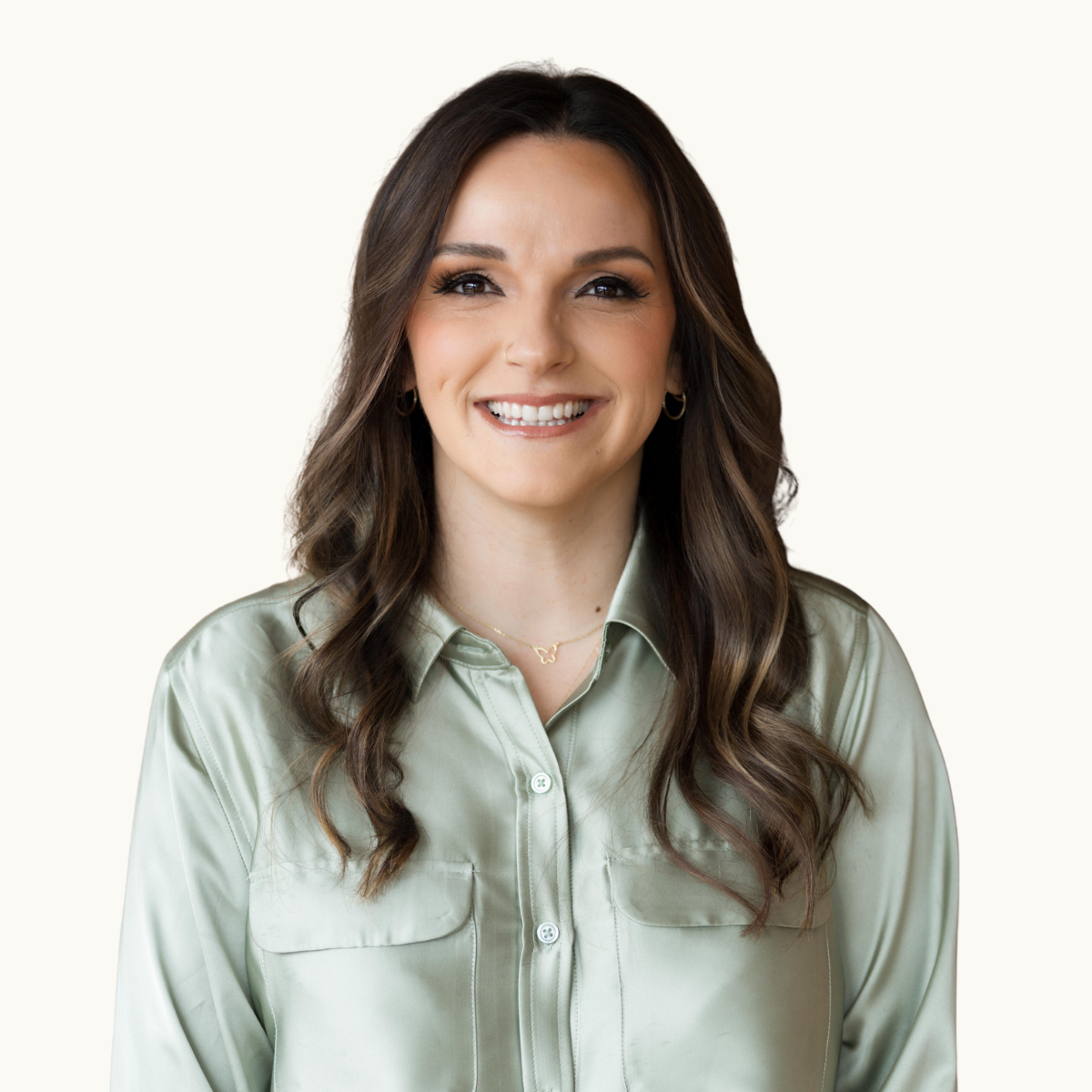 A woman with long wavy brown hair, wearing a light green satin button-up shirt, smiling, against a neutral background.
