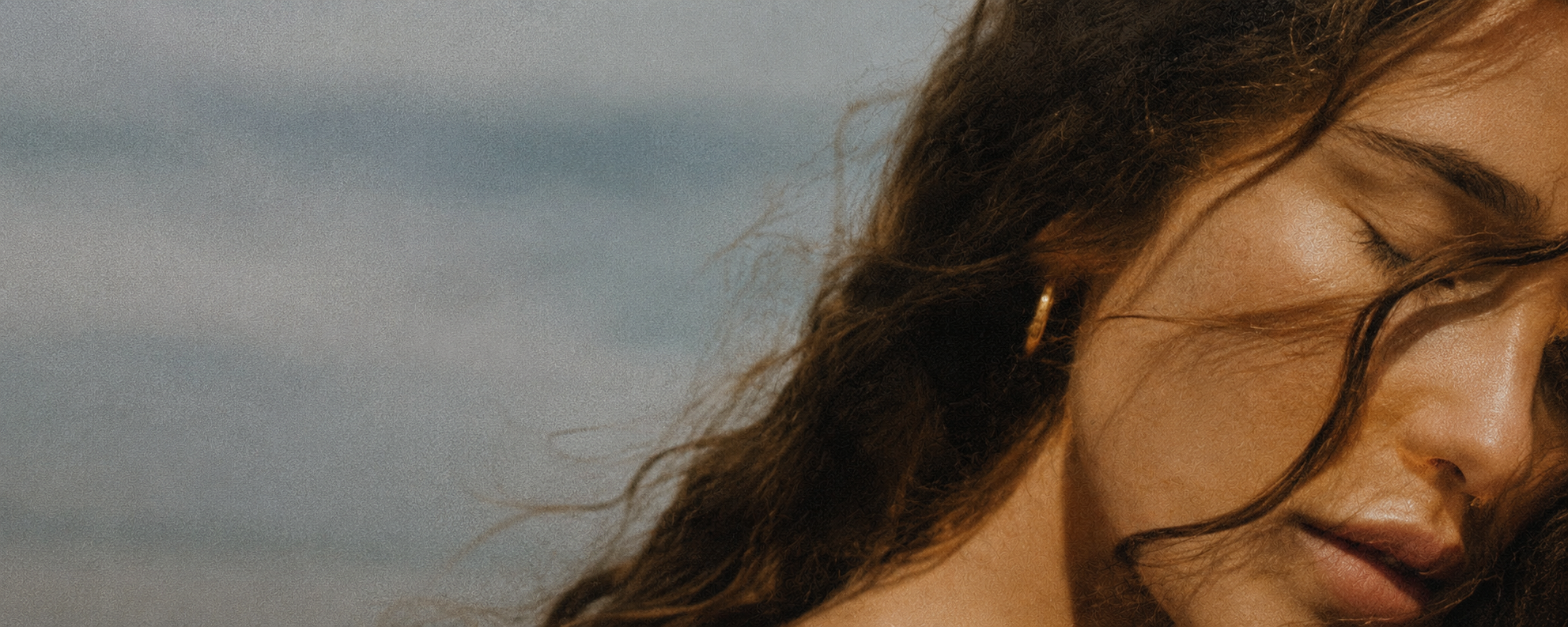 Close-up of a woman with wavy hair and a hoop earring, with her eyes closed and a serene expression.