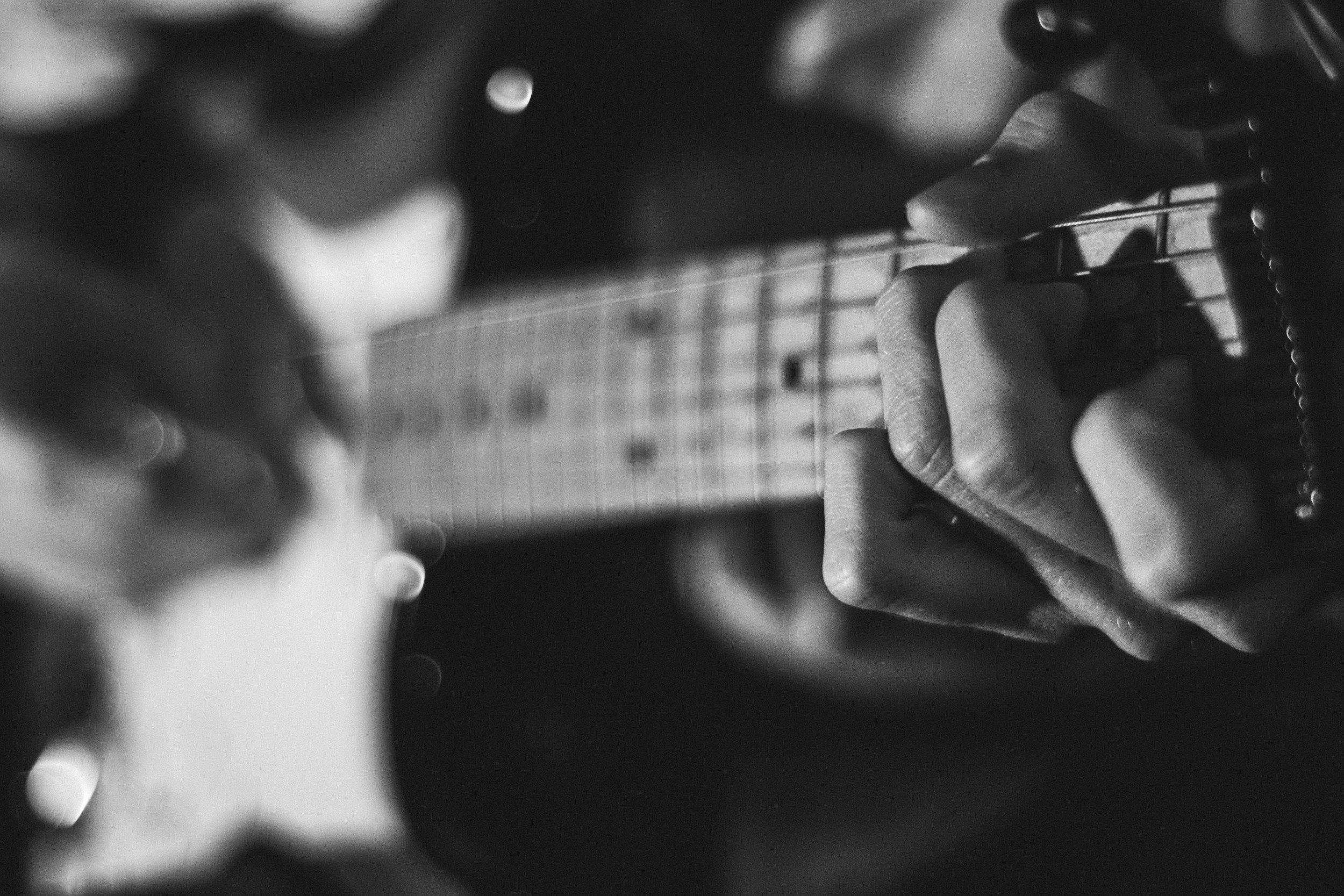 Close-up of a person’s hand playing an electric guitar, captured in black and white.