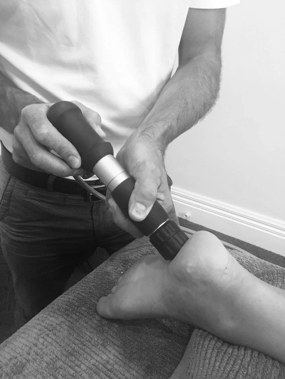 A person using a handheld device to perform a procedure on another person's toe.