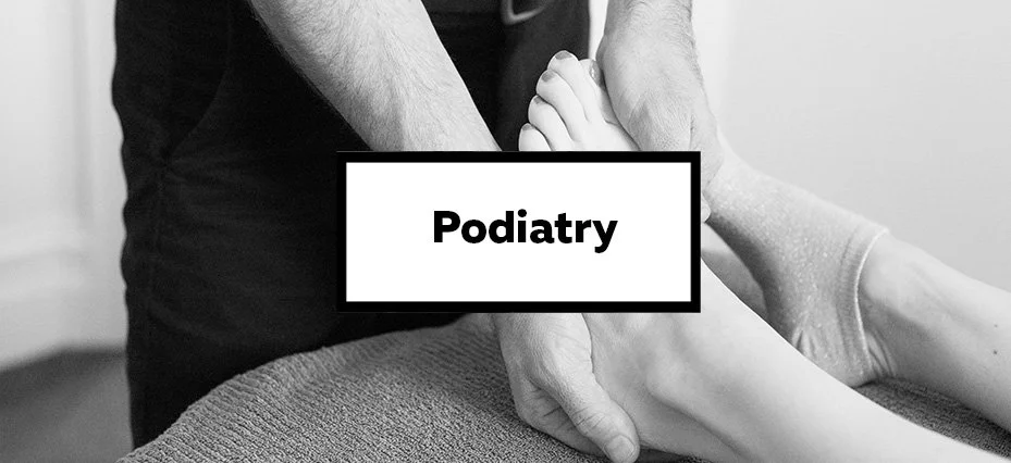 A healthcare provider examining a patient's foot during a podiatry appointment, with a sign labeled 'Podiatry' in front.