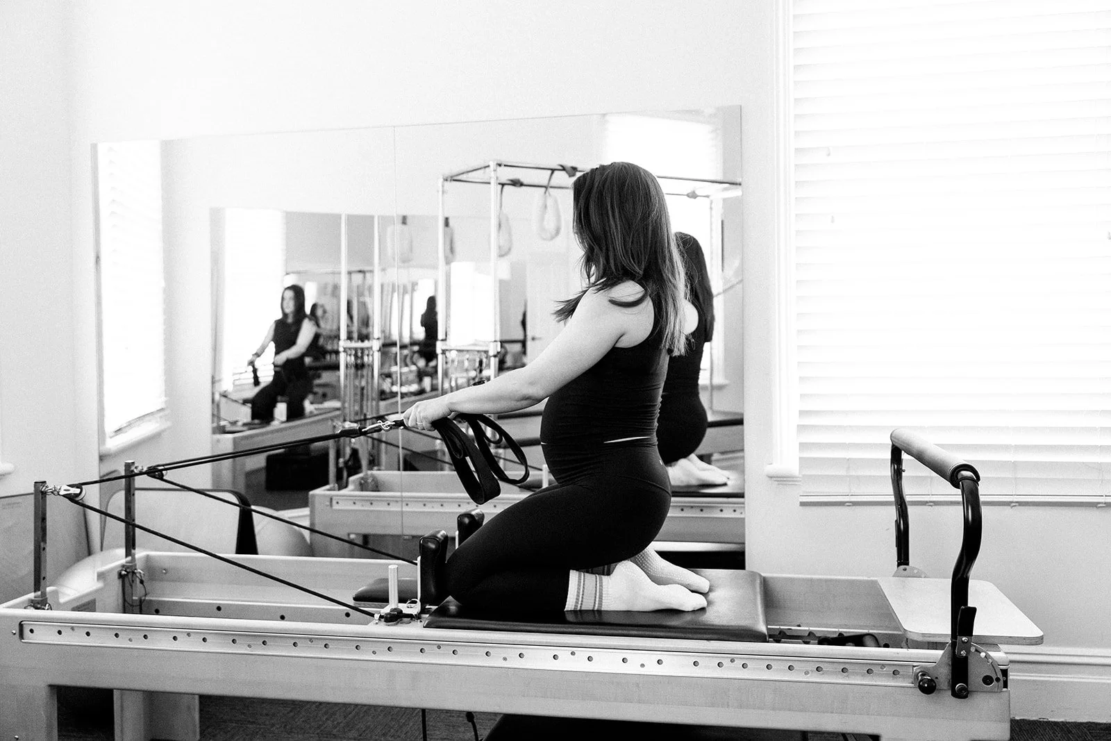 A woman performing resistance band exercises on a Pilates reformer machine in a gym.