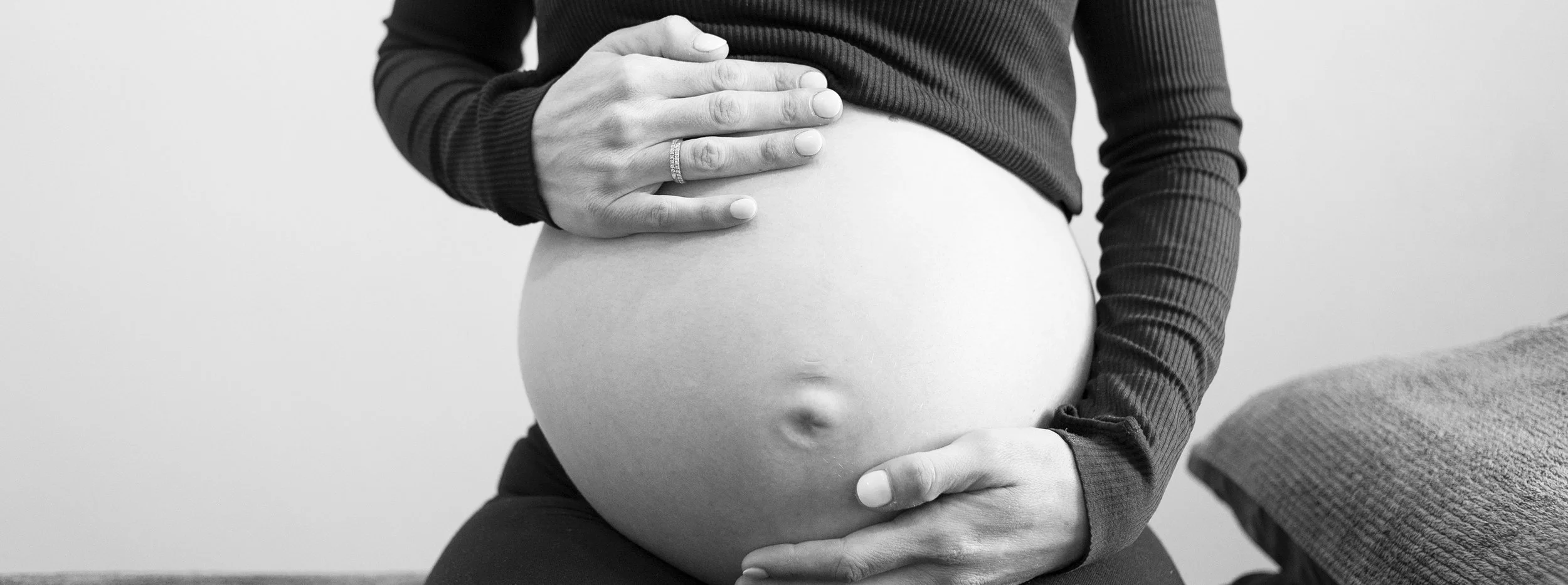 A pregnant woman with her hand resting on her belly, wearing a long sleeve top, in black and white.