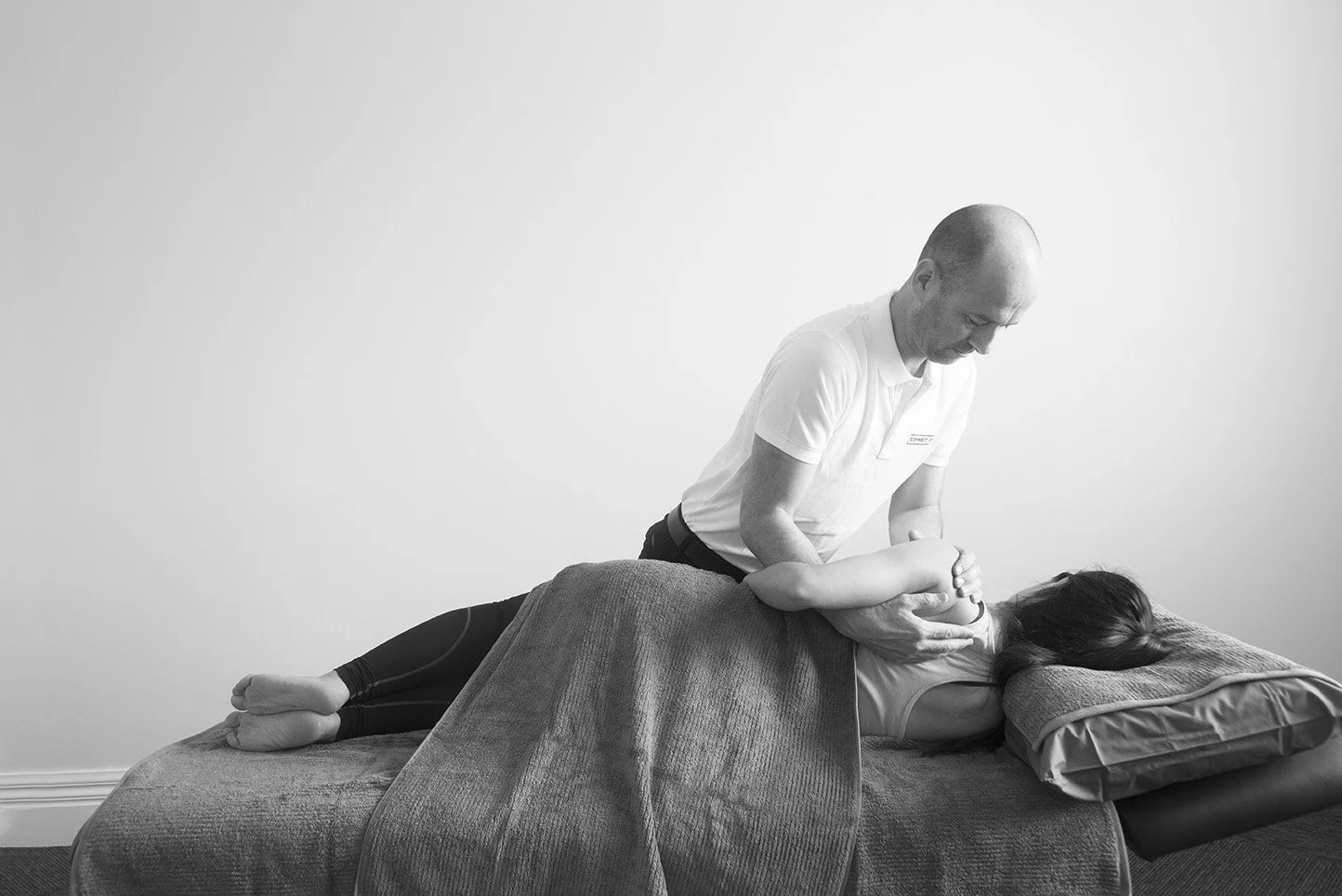 A chiropractor providing a back adjustment to a patient lying face down on a treatment table in a clinical setting.