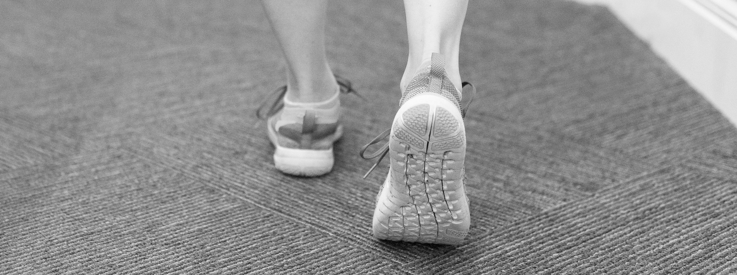Close-up of a person's feet wearing athletic shoes, walking on a textured carpeted floor.