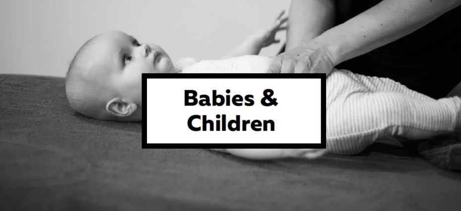 A black-and-white photo of a baby lying on a blanket with a caregiver's hands holding the baby. The text overlay reads 'Babies & Children' in bold black letters inside a white box with a black border.