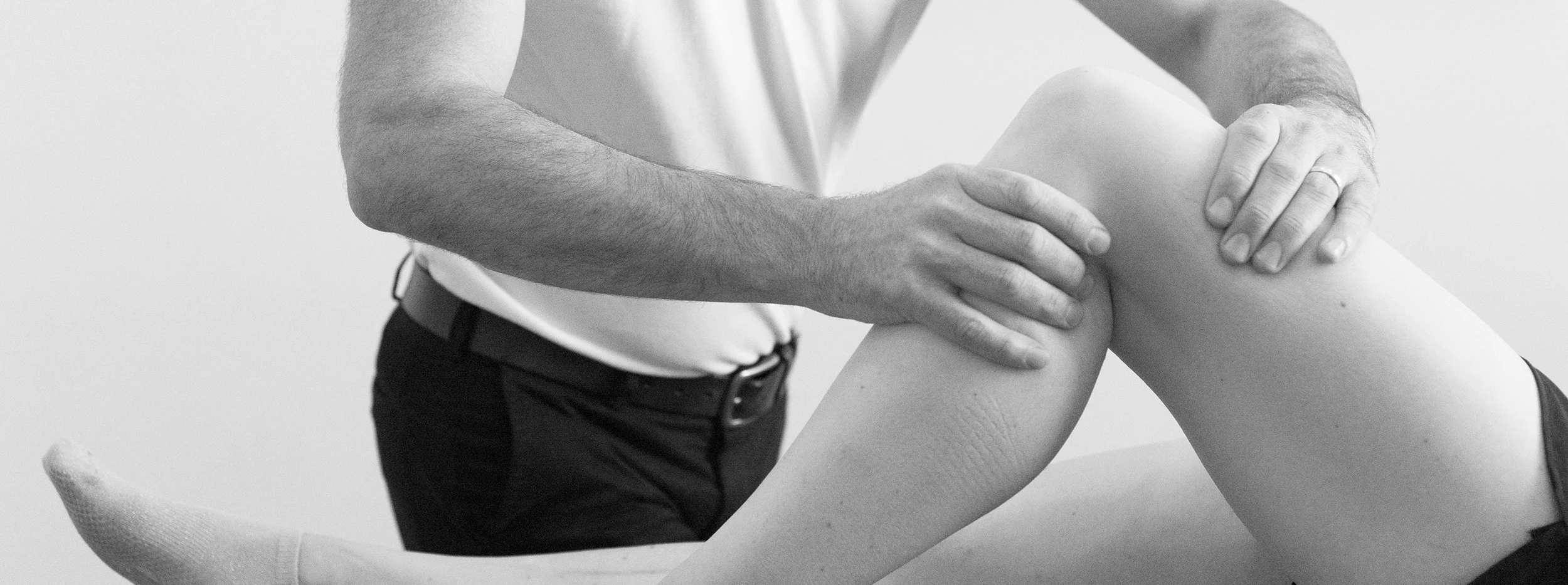 A person with their back to the camera is receiving physical therapy or massage on their knee from another person.