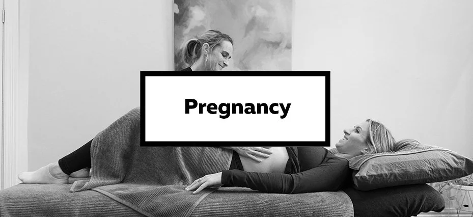 Pregnant woman lying on a bed and another woman leaning over her, both smiling.