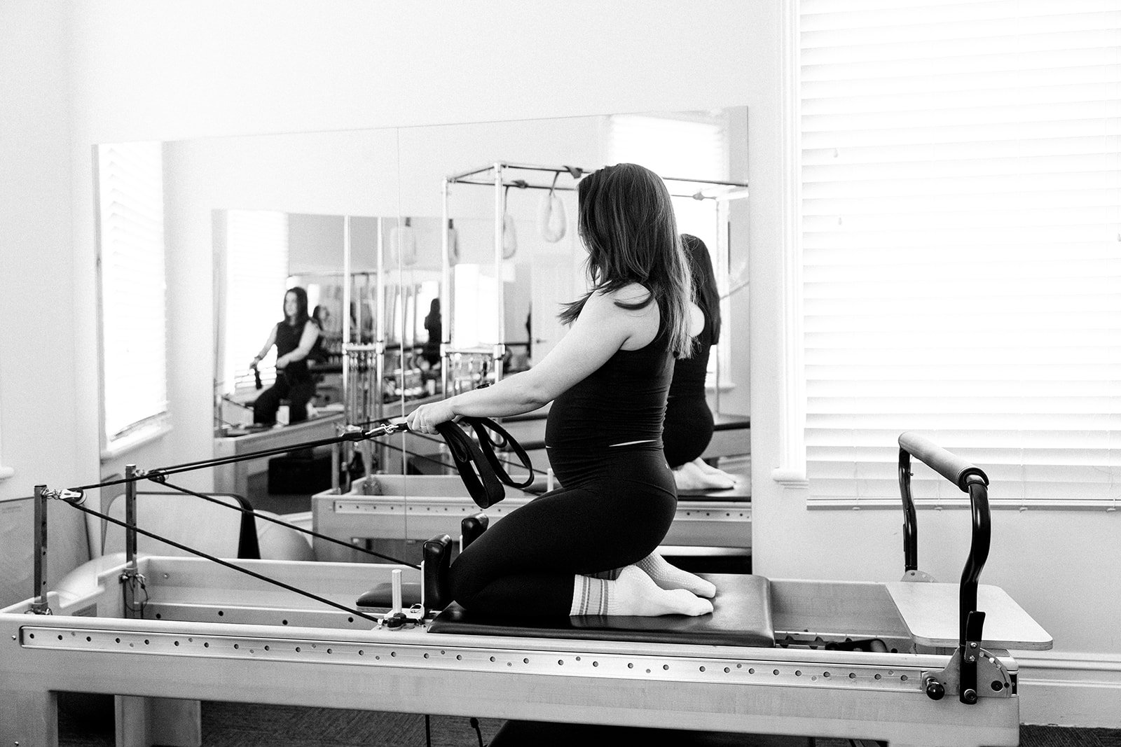 A woman exercising on a pilates reformer machine in a fitness studio.