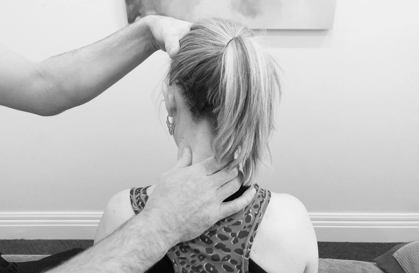 A person with short hair receiving a neck manipulation or massage from a therapist in an indoor setting.