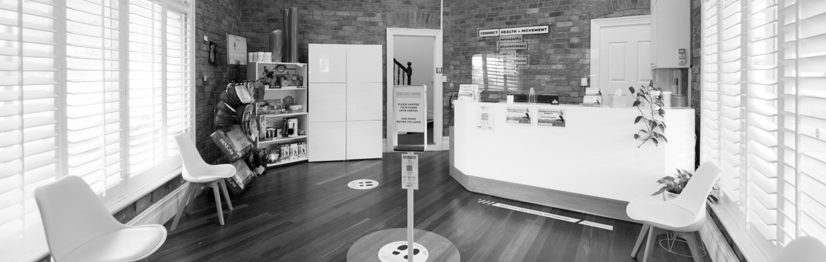 An interior view of a medical or wellness office reception area with chairs, a reception desk, shelves, and signage.
