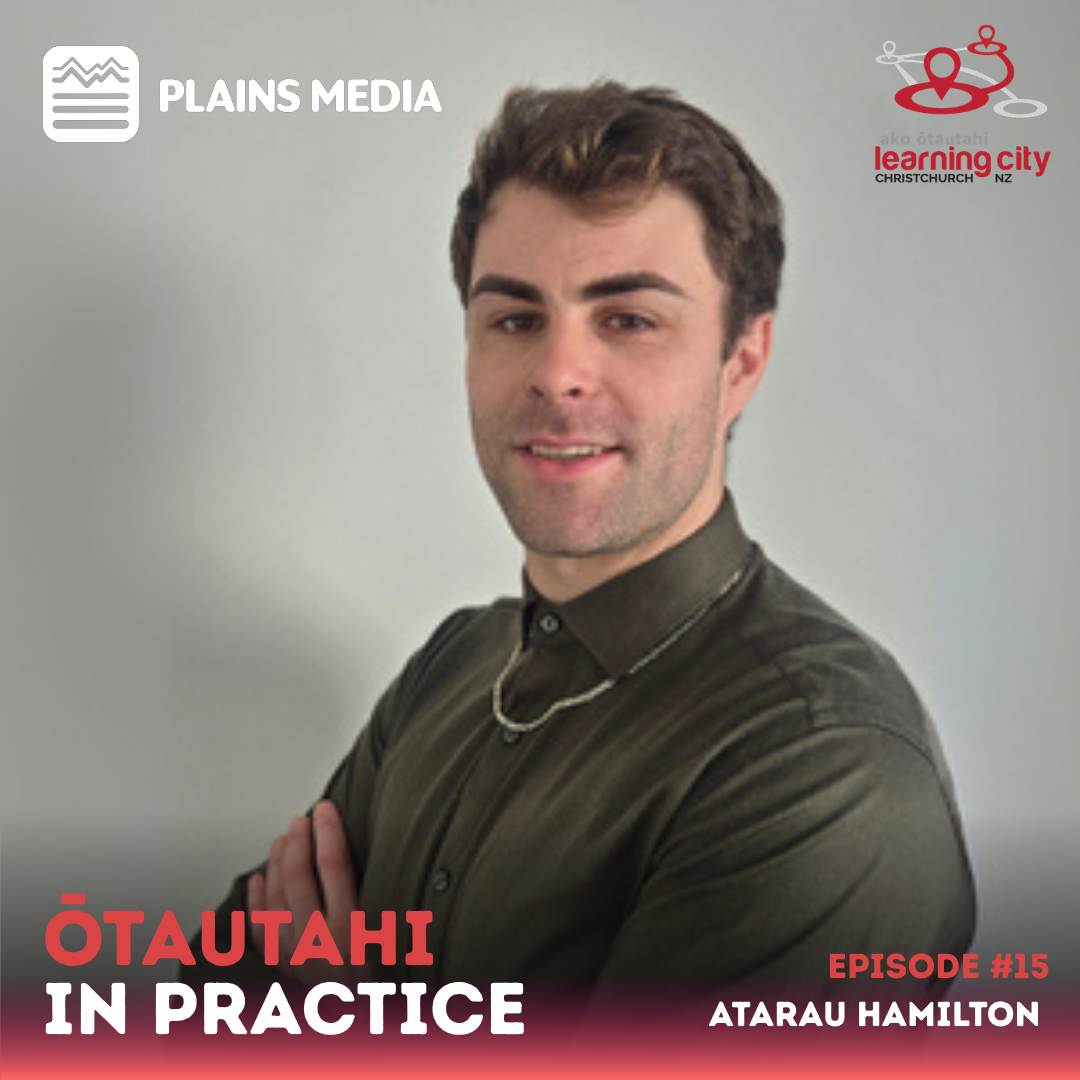 Atarau has turned is head to look at the camera with his arms folded and smiles slightly at the camera.