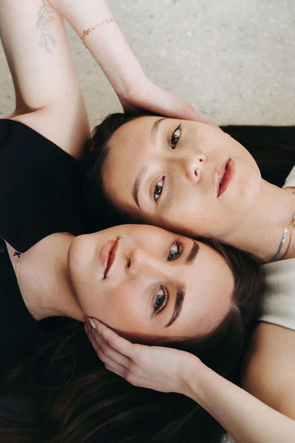 Two women lying close together on a neutral-colored surface