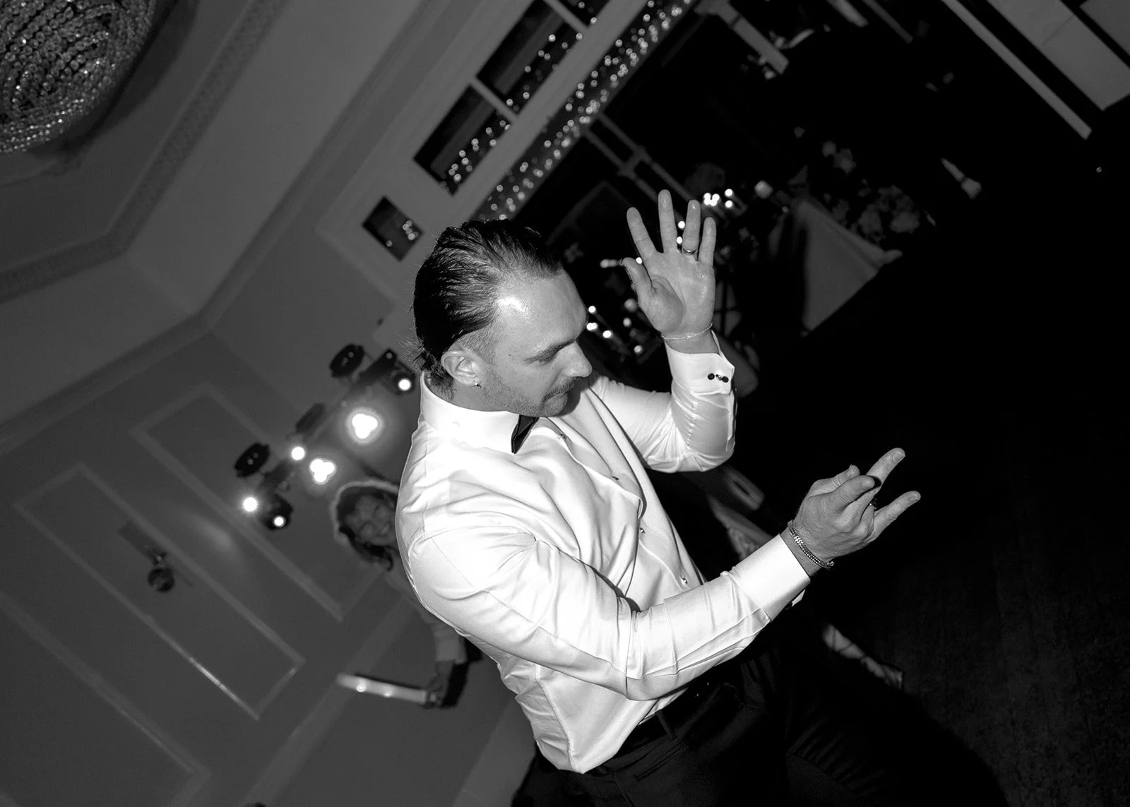 Man in a white dress shirt dancing at a celebration or party with a woman in the background.