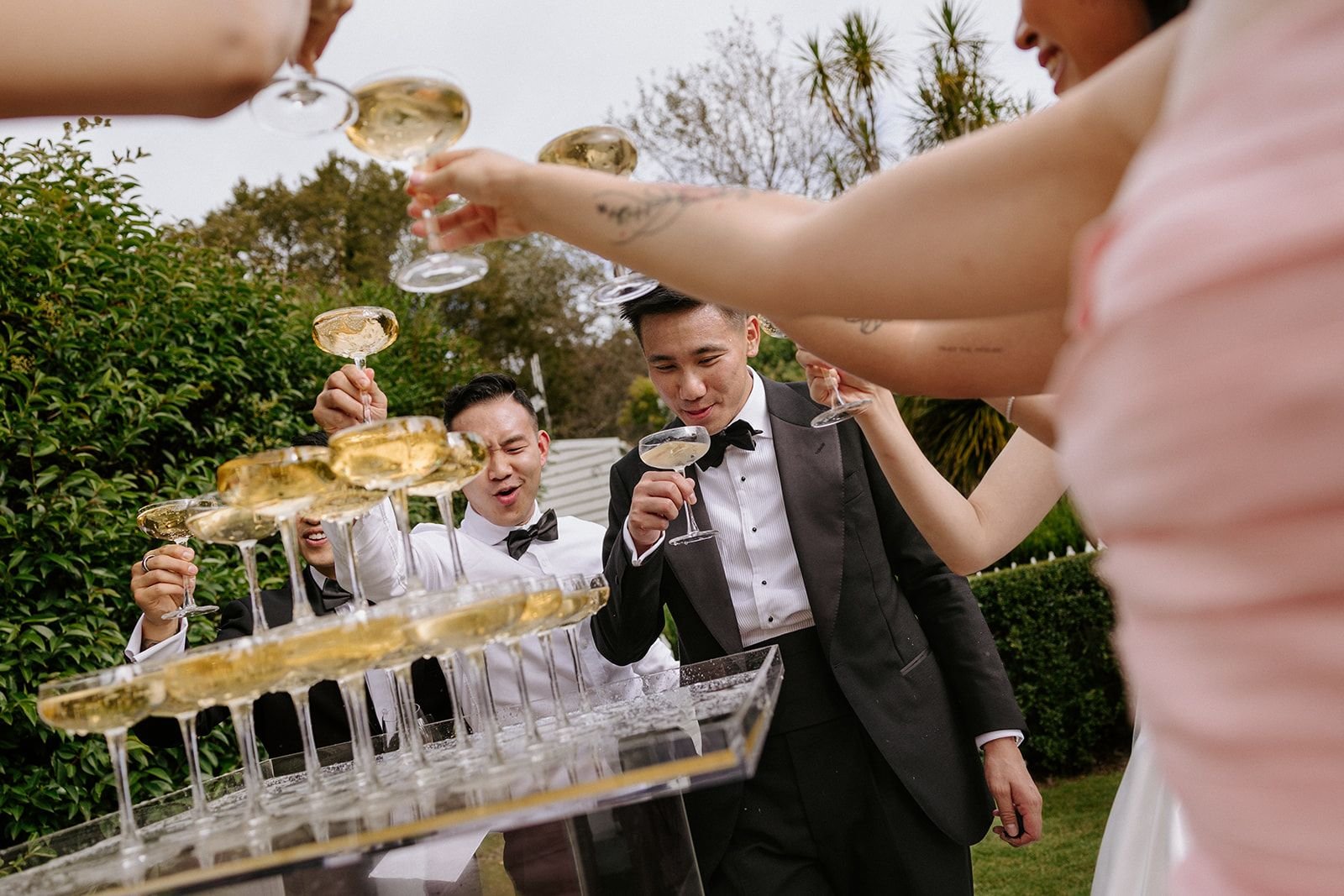People in formal attire raising glasses of champagne for a toast during an outdoor celebration.