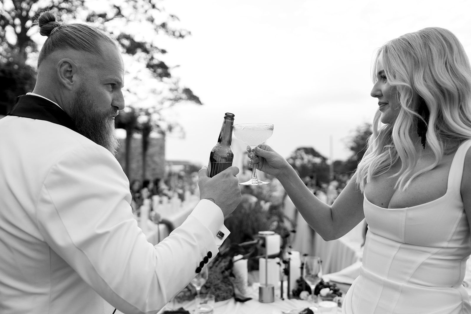 A man and woman at an outdoor wedding reception, toasting with drinks, black and white photo.