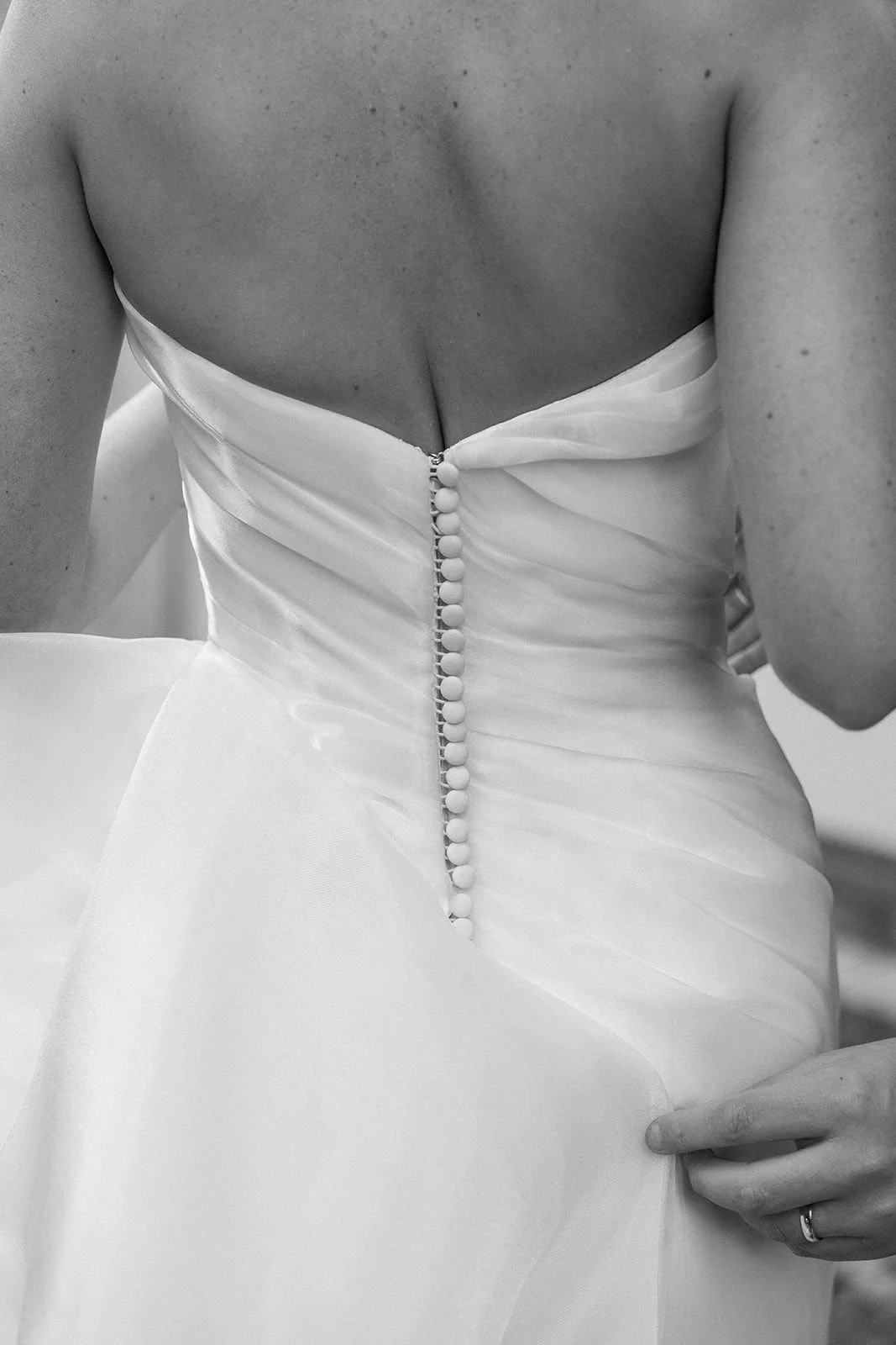 Close-up of a woman in a wedding dress, focusing on the back with buttons and a partially open zipper.