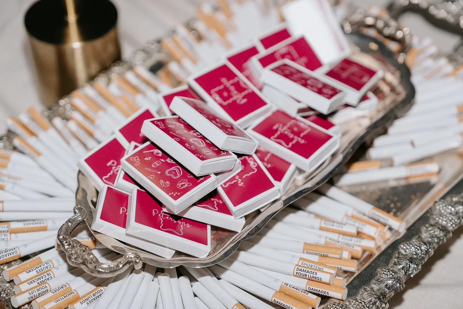 A decorative tray filled with multiple red and white matchboxes and rolled cigarettes, some labeled with warnings about lung damage.
